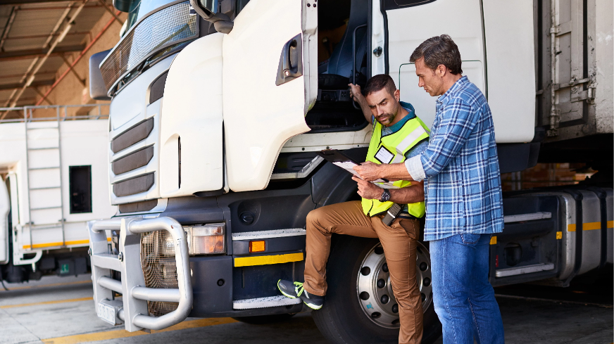 A manager and truck driver check an item manifest before departing